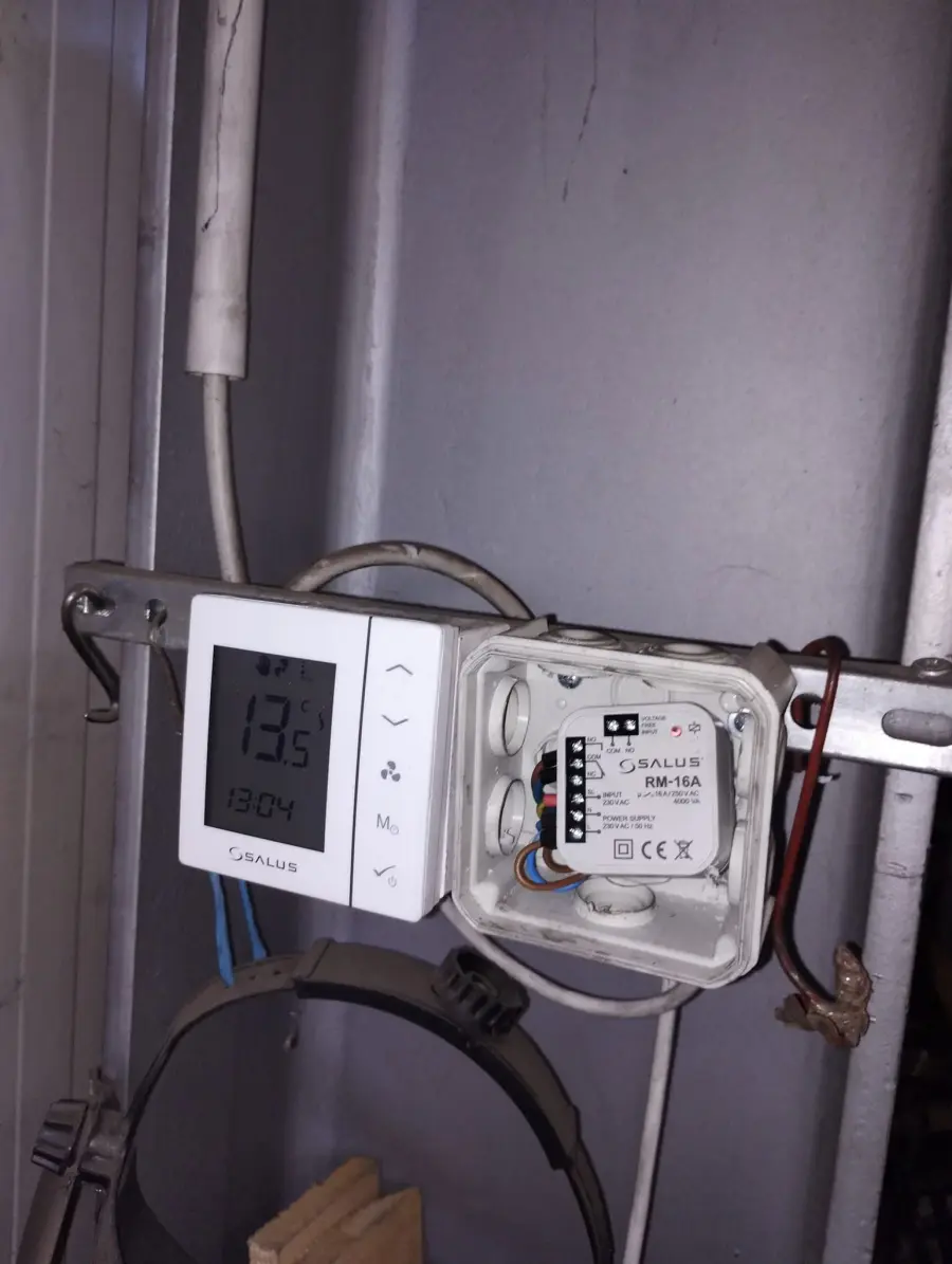Termostat de ambient montat pe perete, alături de modulul de comandă și de conductele instalației