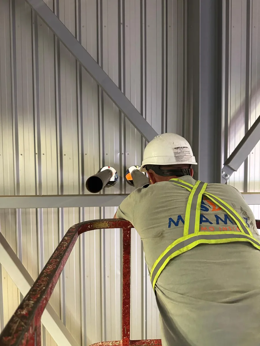 Tehnician montând un racord pe peretele de tablă al unei hale industriale