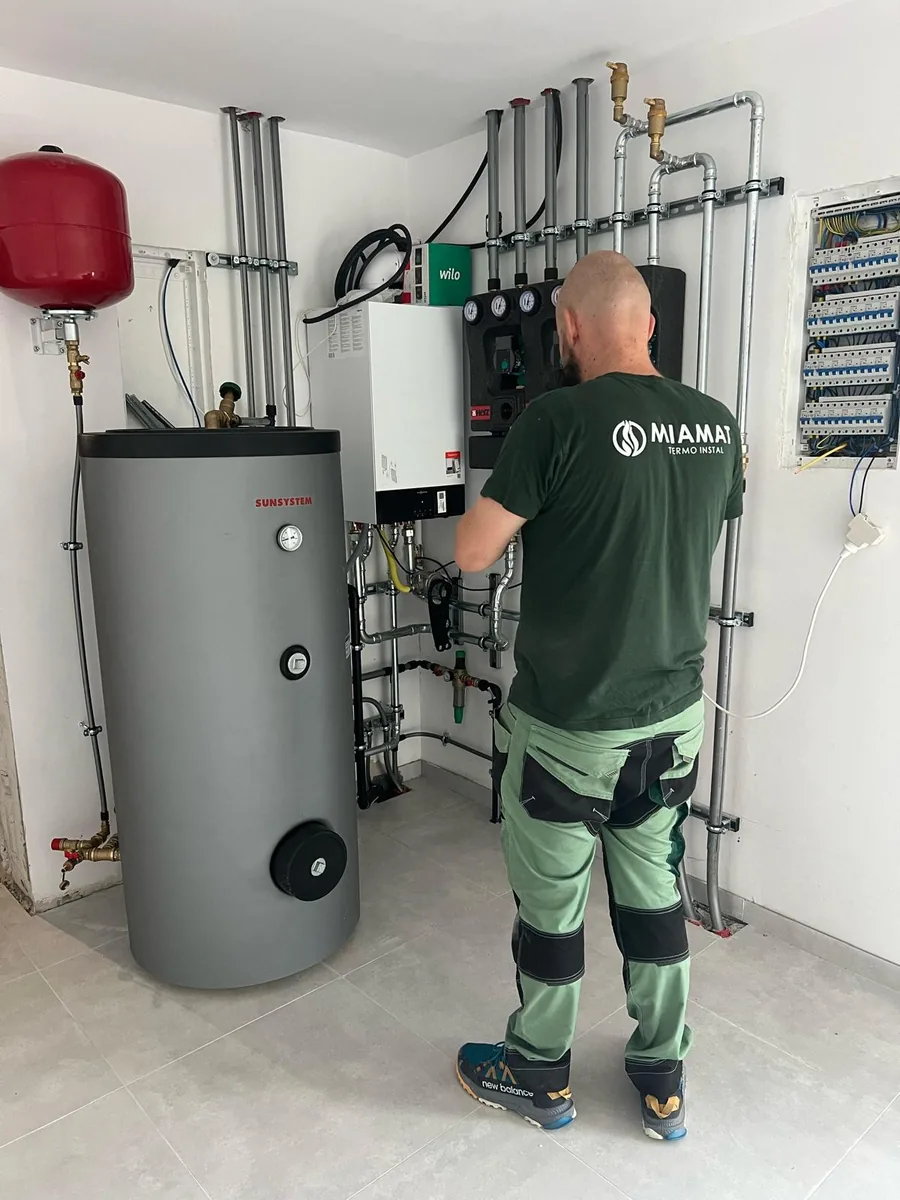 Tehnician Miamat făcând reglajele la boiler și la grupul de pompare, lângă tabloul electric
